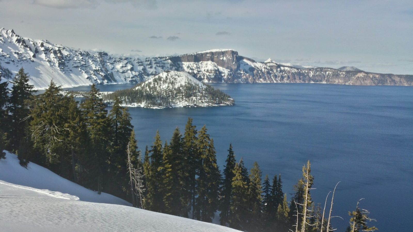 A calm lake beneath forested and snow-capped mountains.
